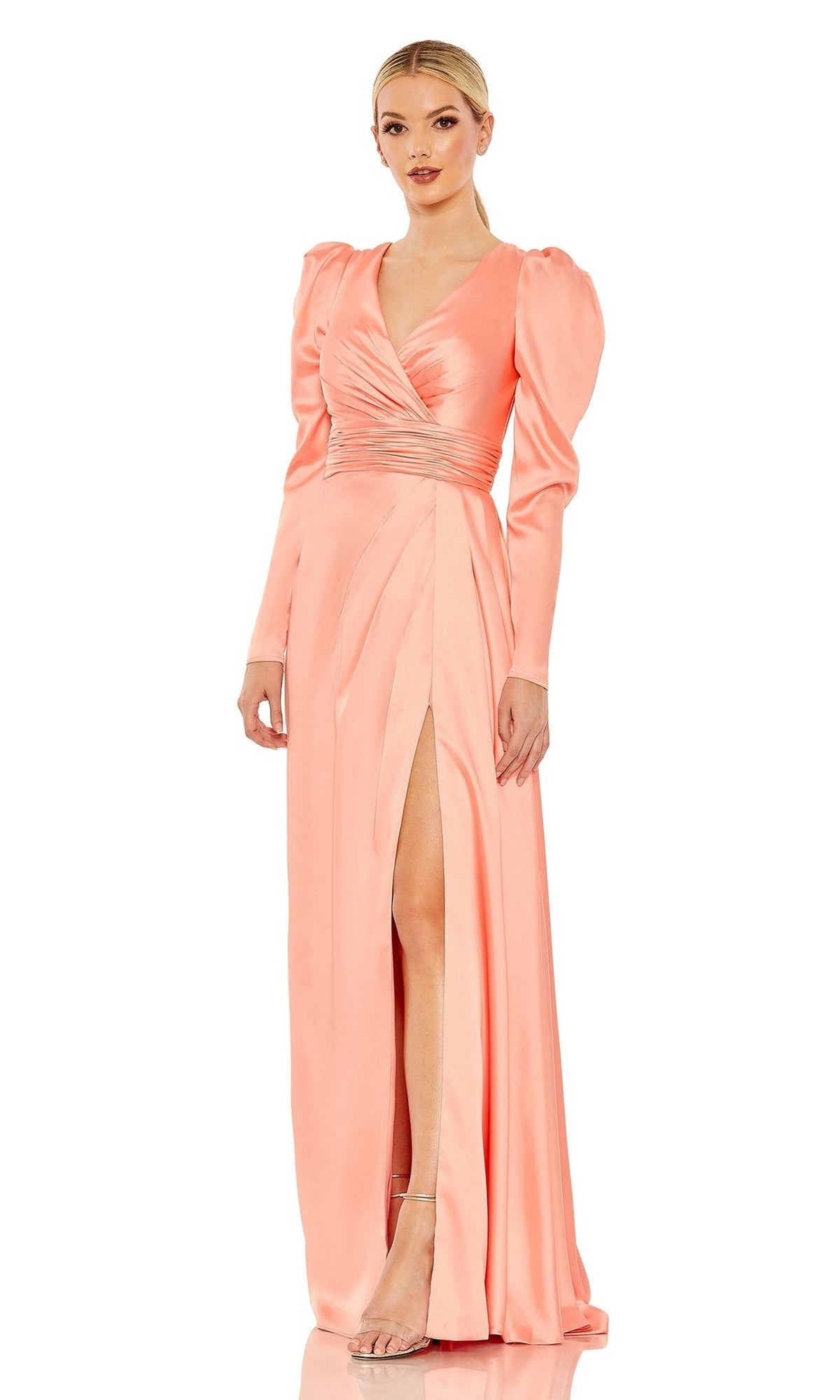 A woman stands against a white background wearing Mac Duggal’s Long Formal Dress 12404, a peach satin gown featuring long sleeves, puffed shoulders, a wrap V-neck bodice, gathered waist, and a high side slit.